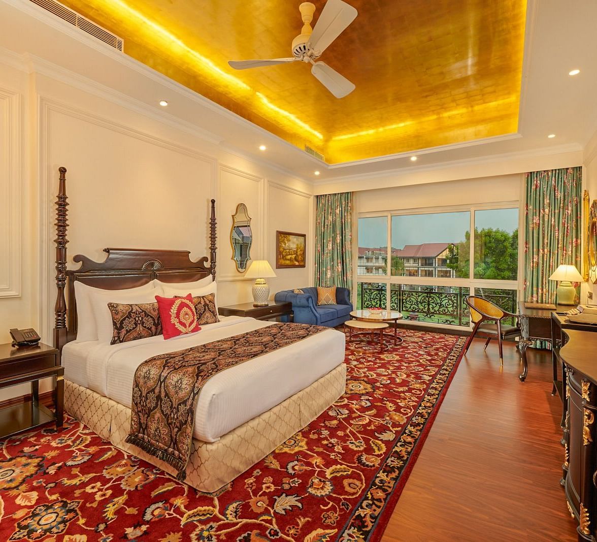 Room with a king bed, golden ceiling, and garden view through French doors.
