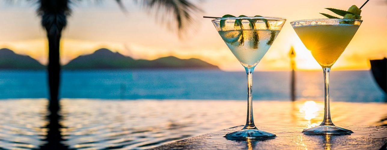 Two refreshing cocktails on a table with a breathtaking sunset view over the ocean in the background.
