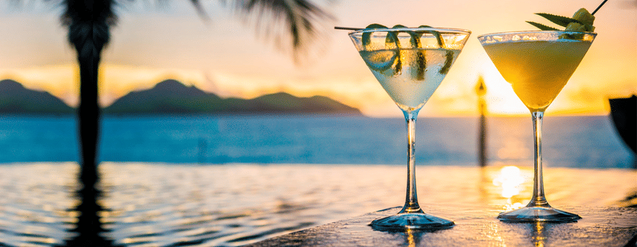 Two refreshing cocktails on a table with a breathtaking sunset view over the ocean in the background.
