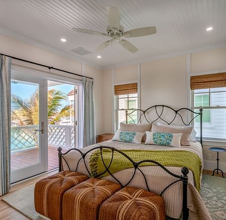 Well lit spacious bedroom with a huge bed on a decorative rug, ceiling fan, windows and a sliding glass door leading to the balcony with a sea view at Abaco Inn.