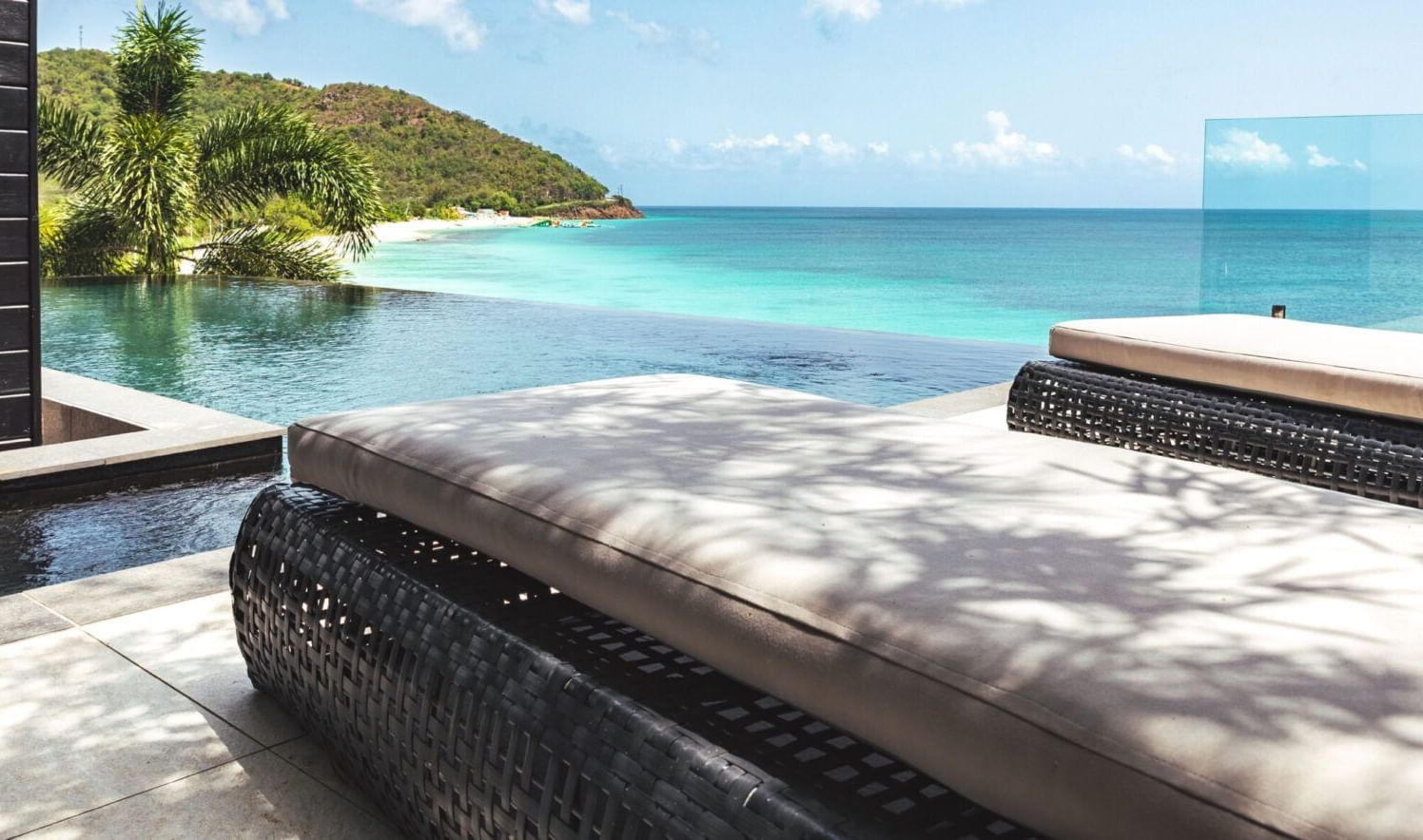 A tranquil infinity pool overlooks a pristine beach and turquoise ocean, with loungers in the foreground and green hills beyond - Tamarind Hills Resort and Villas - Antigua