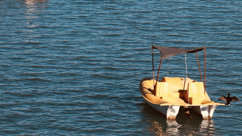2 small boats float on the bright blue, sunlit surface of a lake.