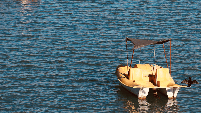 2 small boats float on the bright blue, sunlit surface of a lake.