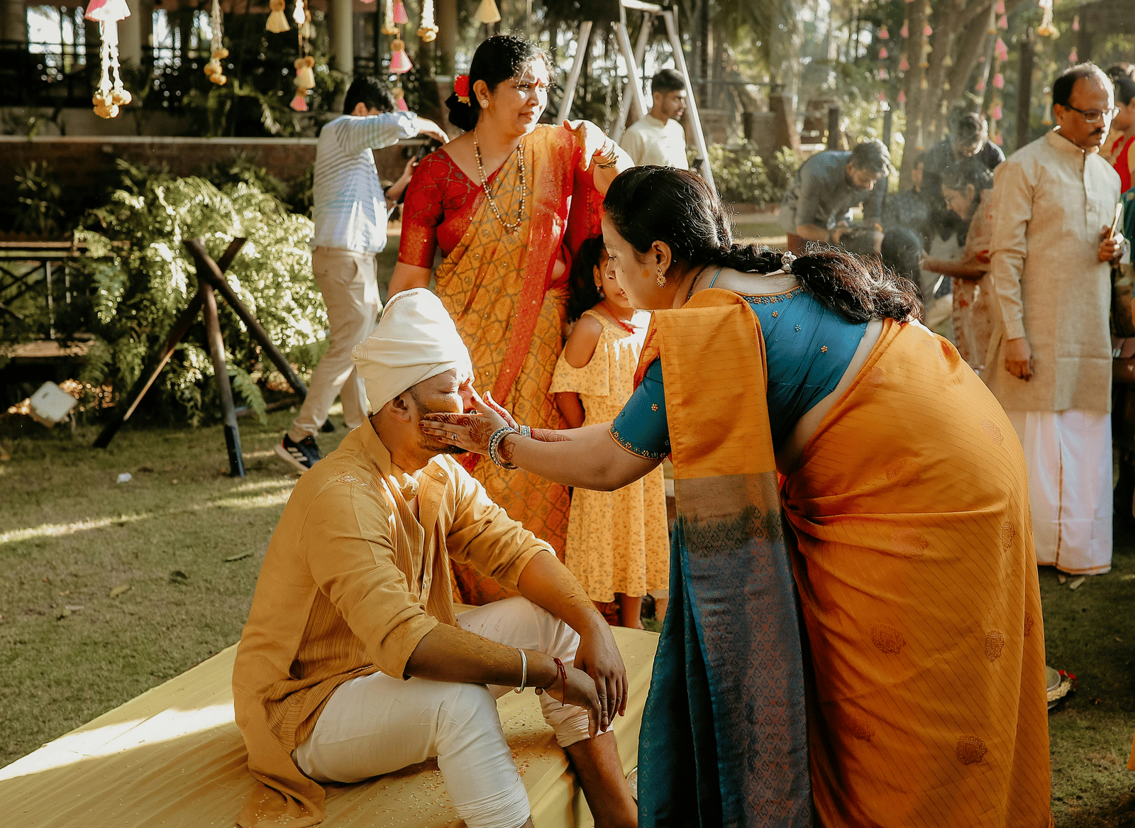 The Indian wedding ritual of haldi being performed in a lawn where a woman is applying turmeric on the groom.