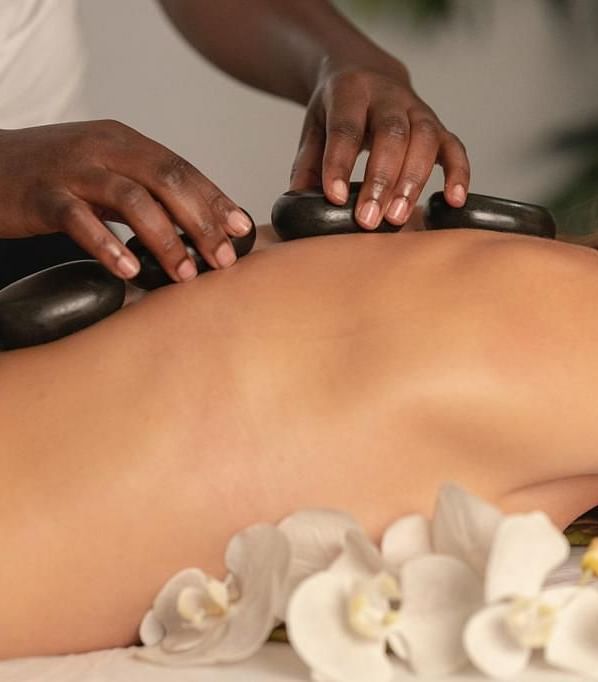 a masseuse placing hot black stones over the spine of a woman lying down over her chest - Historic Tapoco Lodge