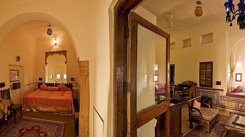 A panoramic view of an elegantly furnished suite at Fort Barli, showcasing arched doorways, a plush bed, and a cosy seating area.