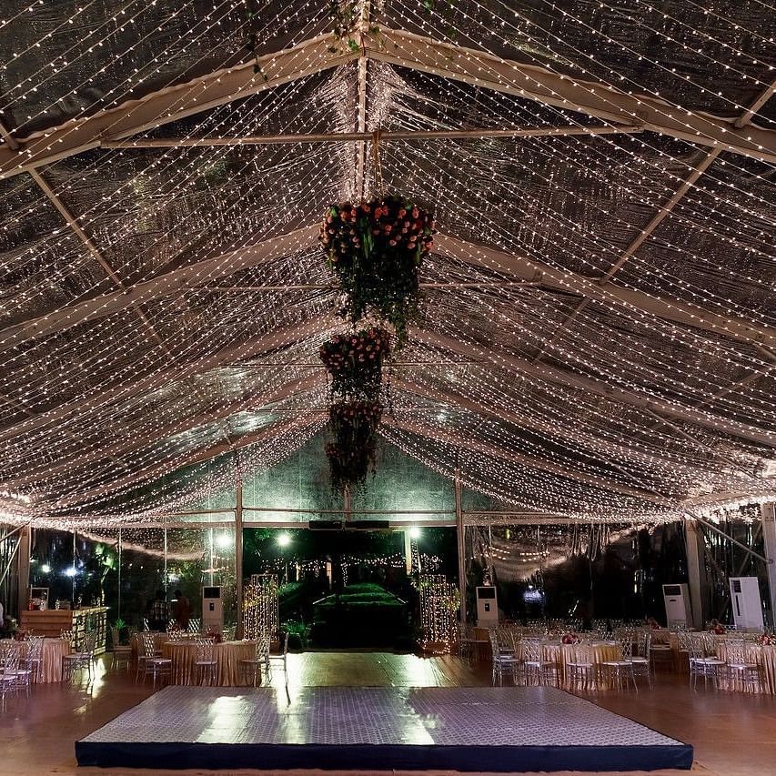 Elegantly decorated indoor event venue with draped lighting, floral chandeliers, and a stage in the center, creating a festive atmosphere at Black Thunder, Coimbatore