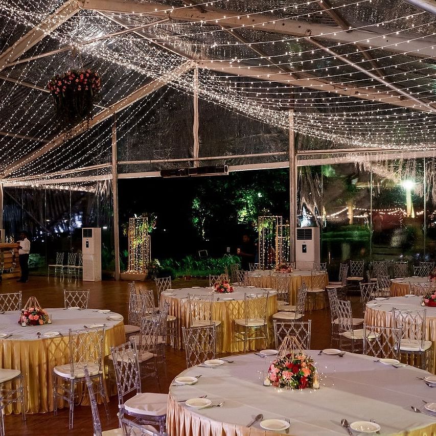 Indoor banquet setup under a beautifully draped ceiling with twinkling lights and round tables elegantly arranged with floral centrepieces at Black Thunder, Coimbatore
