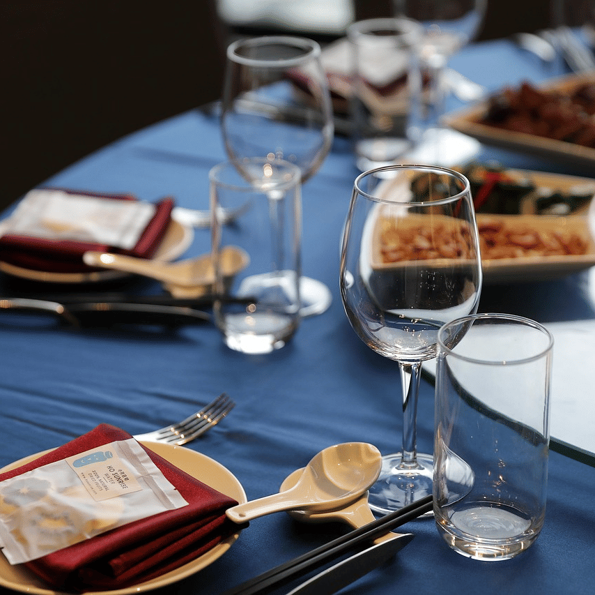 A close up shot of a round dining table with sparkly glassware and cutlery arranged on it.