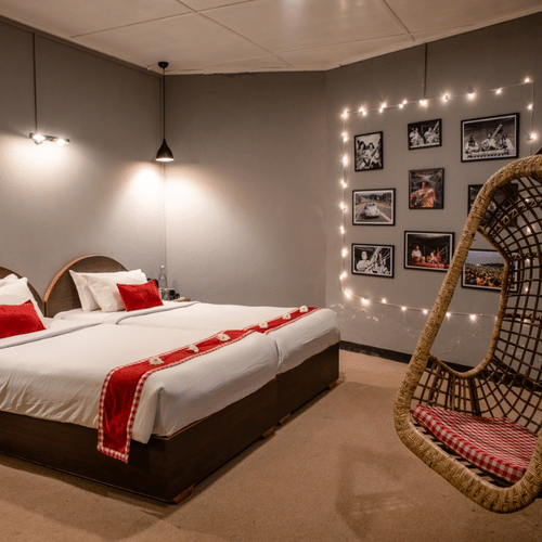 A room at Woodstock Farmhouse, Shillong, featuring a large bed, bedspreads, pillows, swing, and wall art.
