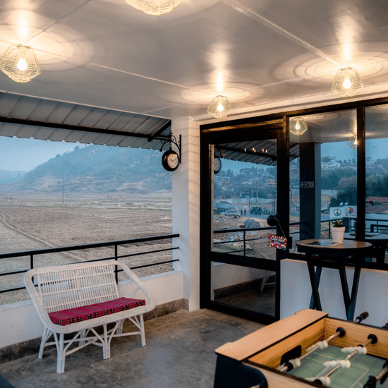 Covered balcony lounge at Woodstock Resort with seating, a foosball table, hanging lights, and large windows overlooking hills and an open landscape.