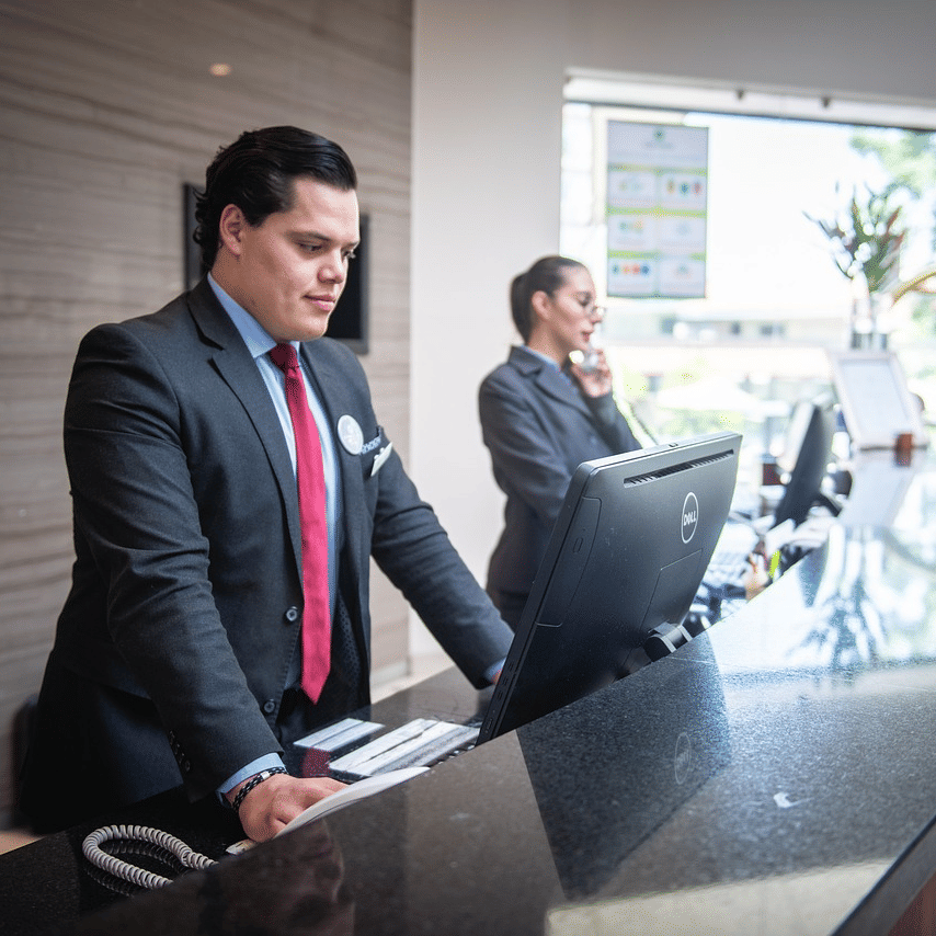 Two staff members standing behind the reception desk dressed in business formals.