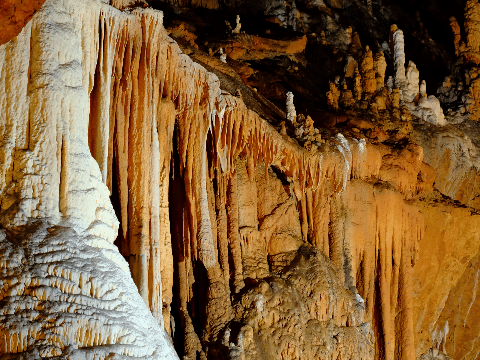 Striating mineral flowstone and stalactites cover the warm brown walls of an underground cave.
