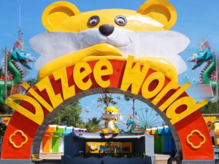 MGM Dizzee World gate with colourful activities area at the background flanked by green trees.
