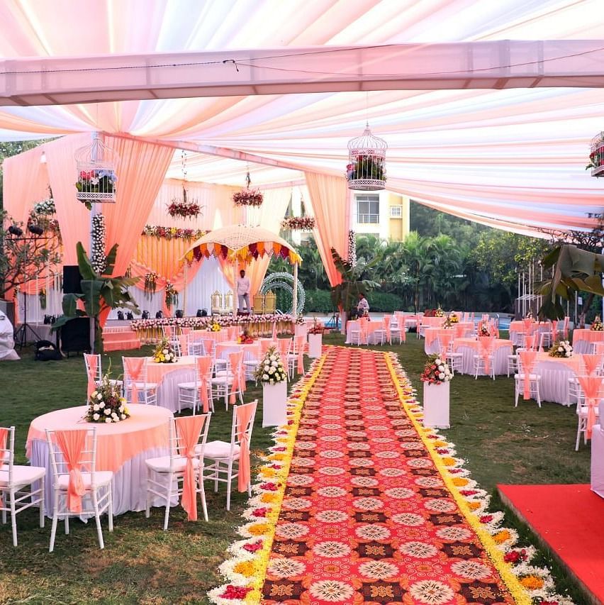 alt-text A well decorated wedding lawn with cloth and floral decors on round tables and chairs, with a decorative carpet on the floor.