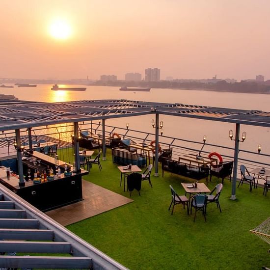 A bar counter on a rooftop terrace during sunset, showcasing a selection of alcohol bottles and a river in the background.