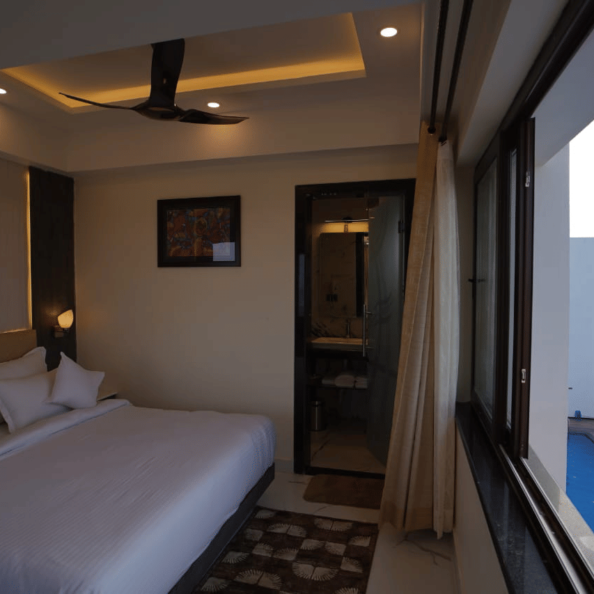 Bed positioned opposite a massive glass window in one of the rooms at Shanti Seaview Resort & Spa, offering natural light and scenic views.