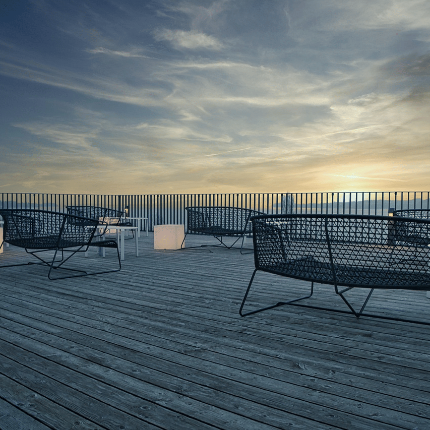 A terrace featuring a wooden deck with a few benches facing towards the beautiful sunset.