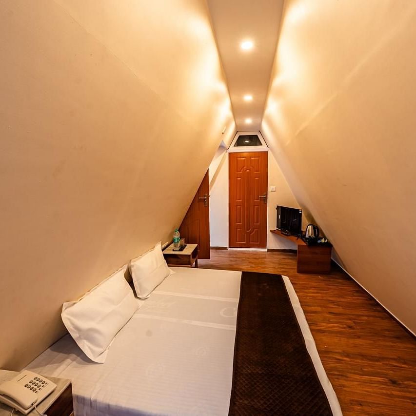 A hotel room with angled walls creating a narrow appearance, a bed, and a television visible at the far end.