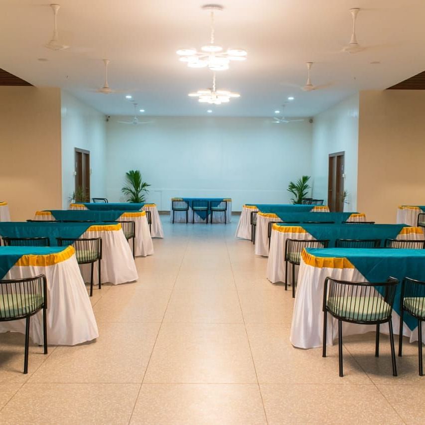A banquet hall set up for an event with tables and turquoise table cloths - Lords Eco Inn Belagavi