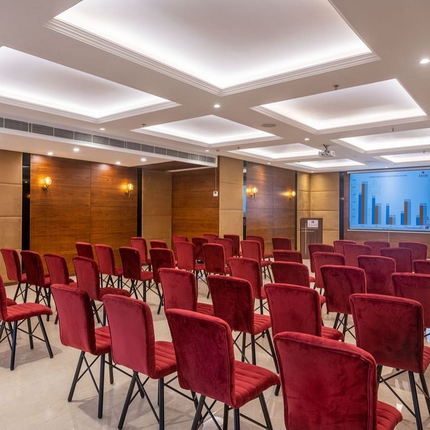 Mid-size conference room with rows of red chairs facing a presentation screen.