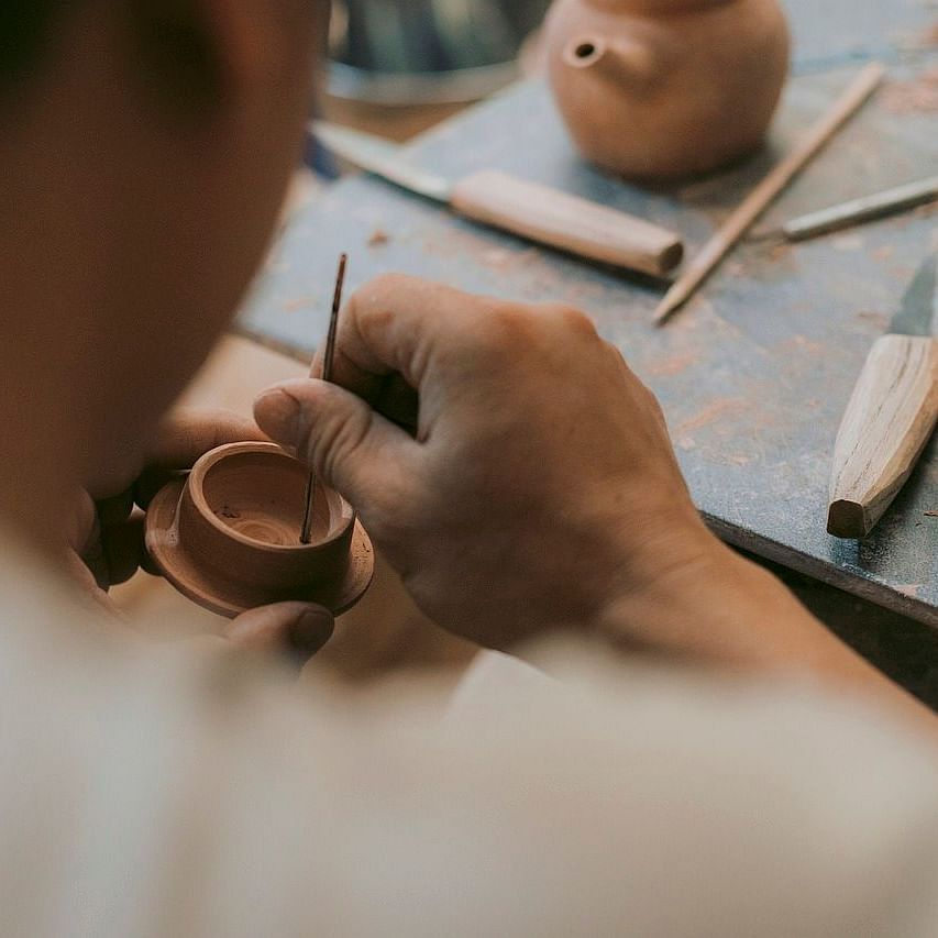 Close-up of a person shaping pottery with tools on a worktable, surrounded by clay and crafting tools.