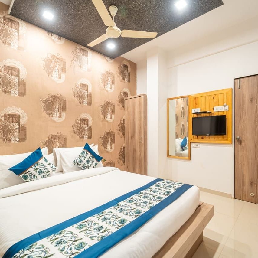 Standard Room featuring a bed with blue accents, patterned wallpaper, and a television.