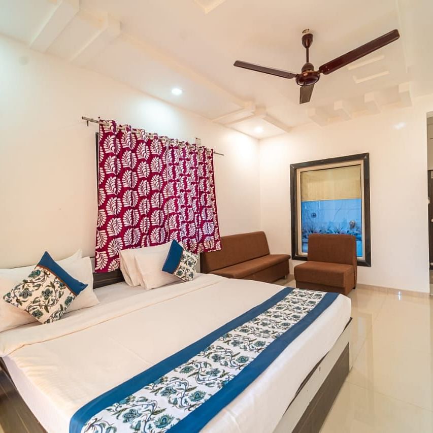 Deluxe Garden View Room showcasing the bed with blue and white linens, a decorative headboard, a patterned screen, a ceiling fan, and a glimpse into an adjacent area.