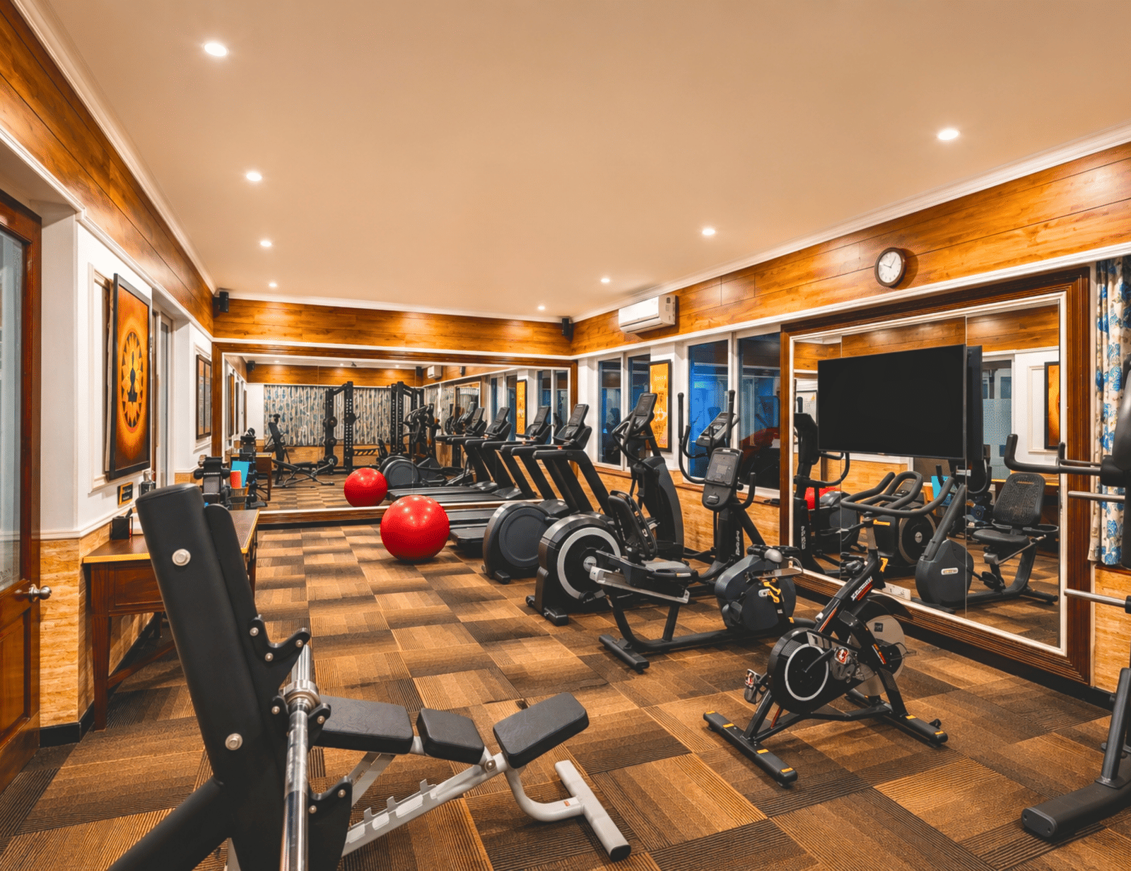Fitness centre with treadmills, exercise bikes, a weight bench, stability balls and a wall-mounted television at MAYFAIR Palm Beach Resort, Gopalpur-on-Sea.