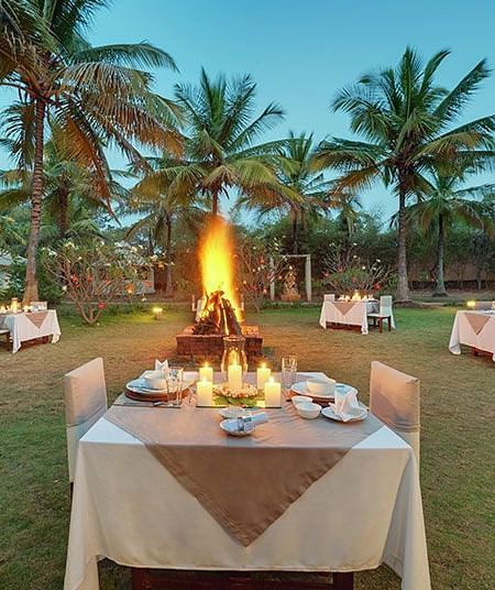 A beautifully arranged outdoor dining setup near a bonfire with a beach view - Shreyas Retreat