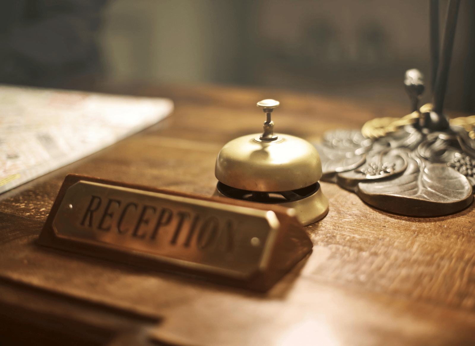A brass service bell, and a rectangular brass 'RECEPTION' plaque sit on a polished wooden desk.