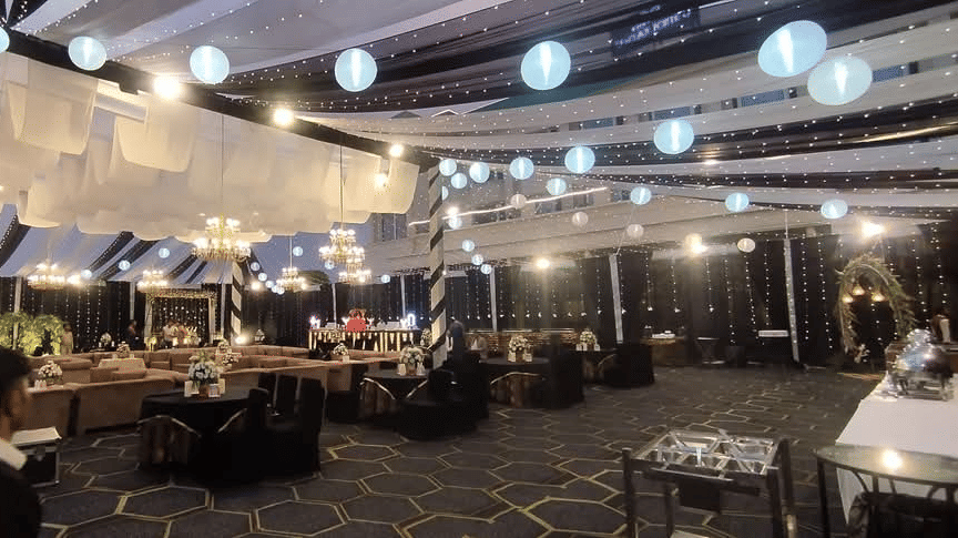 Stylish evening event space at Ambrosia Sarovar Portico, Haridwar, with seating, hanging lanterns, chandeliers, and soft ambient lighting under a decorated canopy.