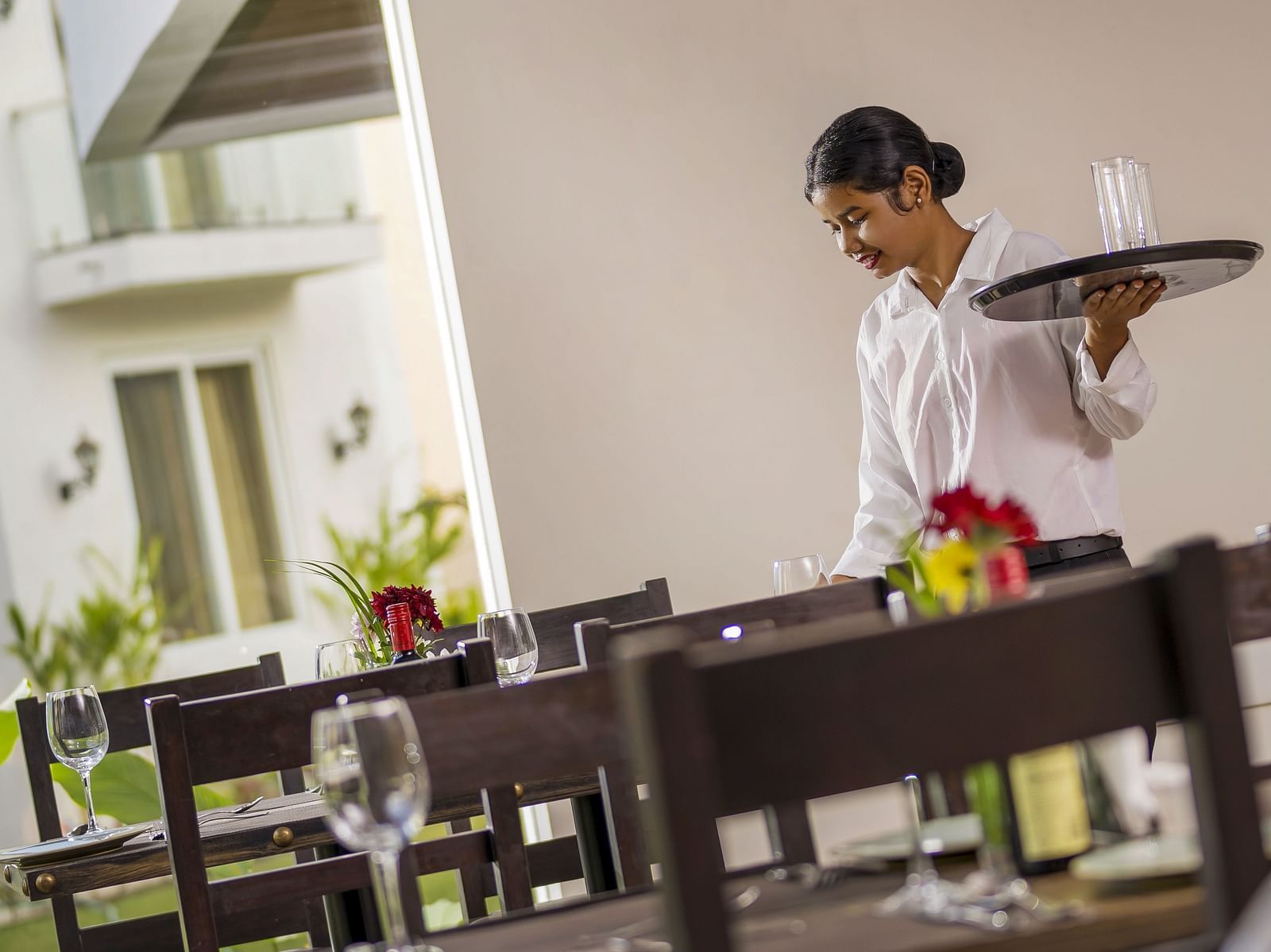 a staff member looking down while holding a tray with a glass in it - The Tanisi Hotels & Resorts, Goa