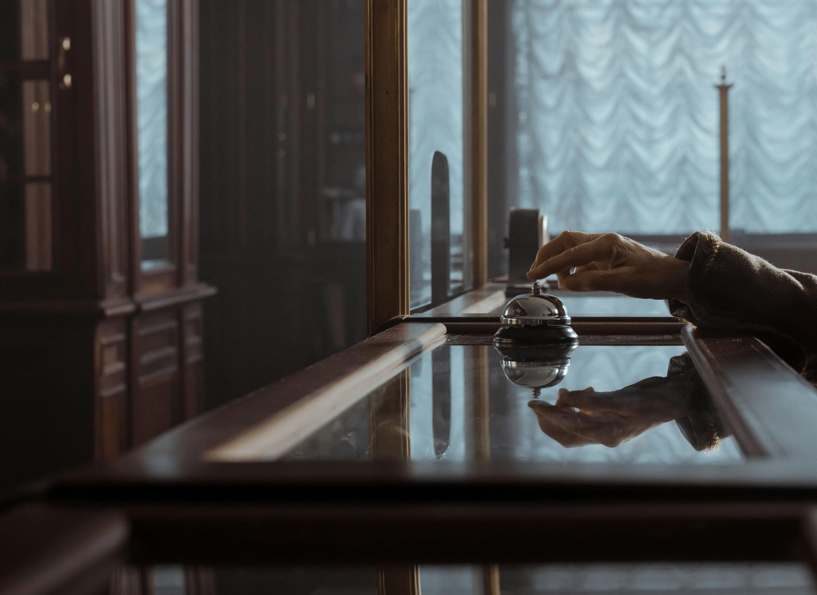 A close-up shot of a person using a laptop on a wooden table near a window with sheer curtains.