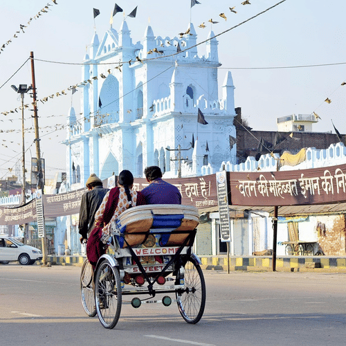 A cycle rickshaw carrying 2 passengers on an empty roan in Lucknow passing by a mosque.
