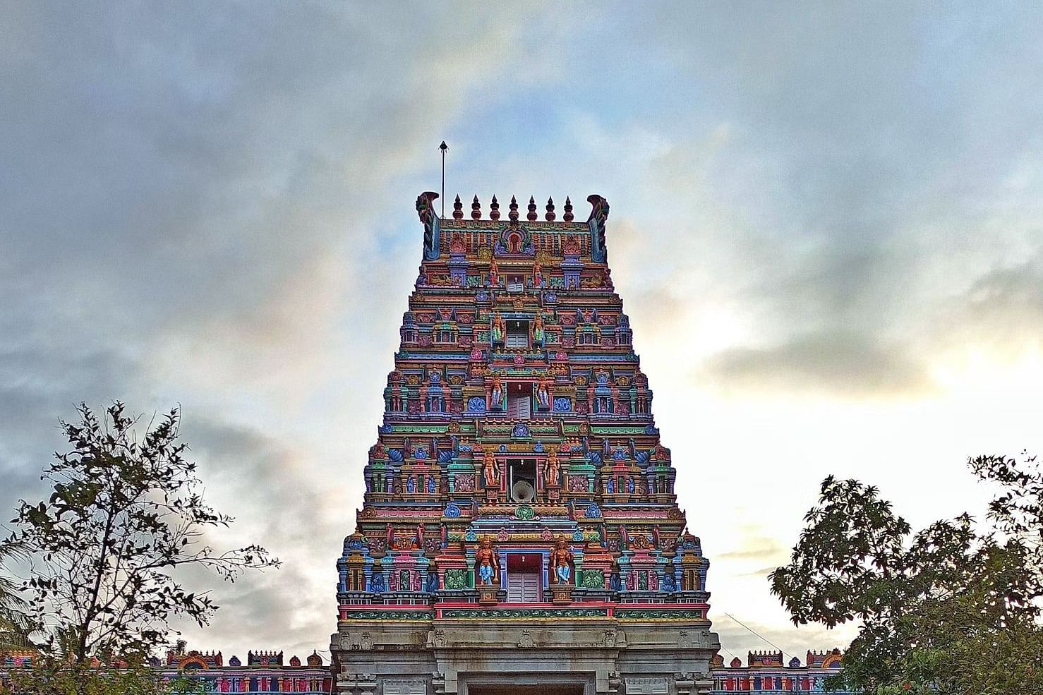 Wide view of a multicoloured South Indian temple tower under a cloudy evening sky.