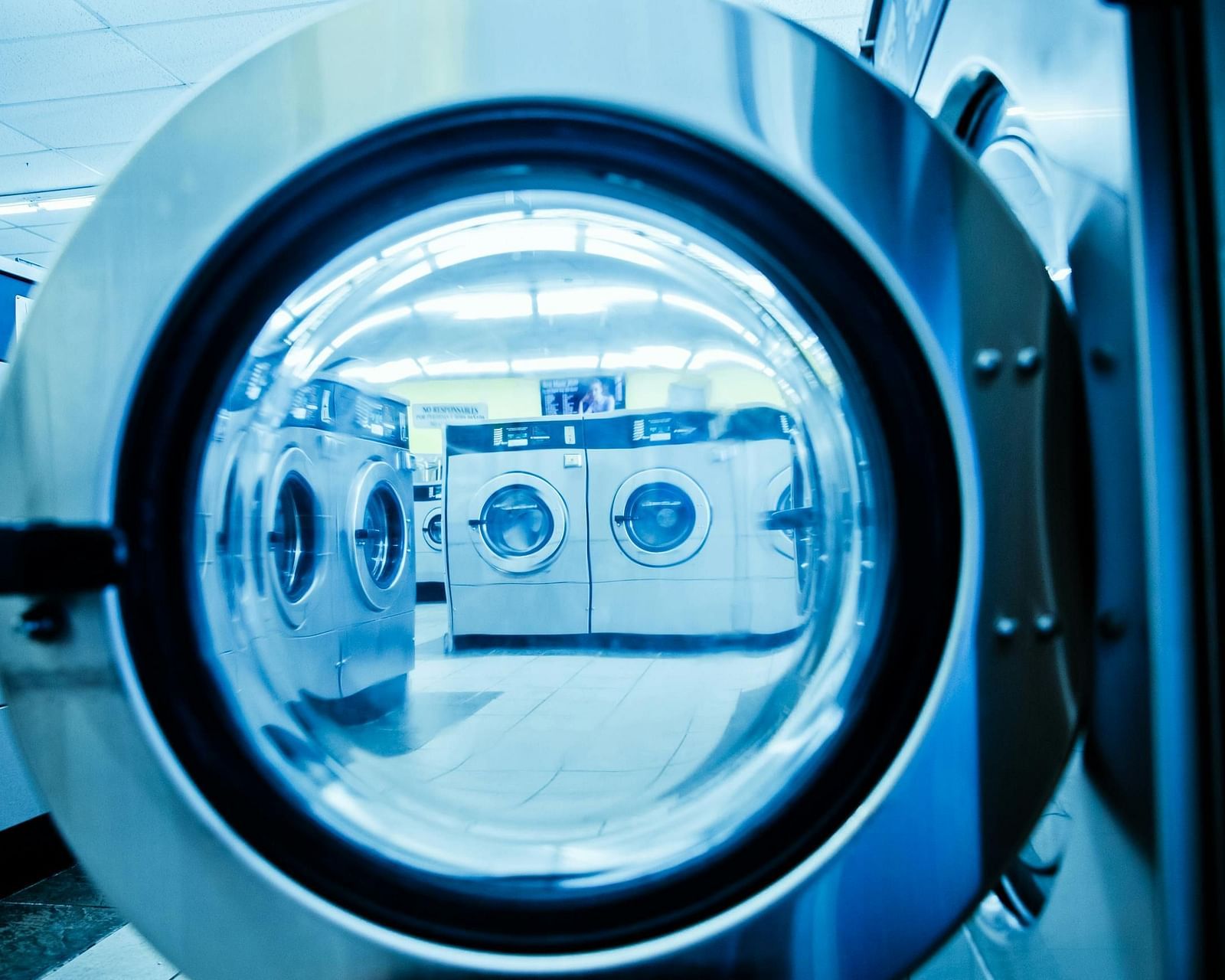 A close-up view of the open door of a commercial washing machine, reflecting other washing machines inside.