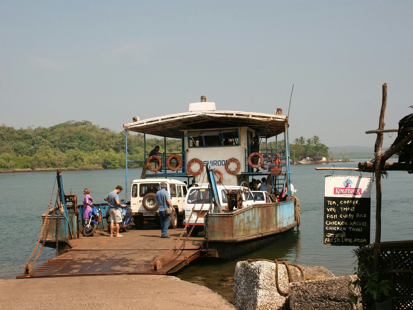 A ferryboat at a dock on a calm river, loading people and vehicles under a clear, bright sky