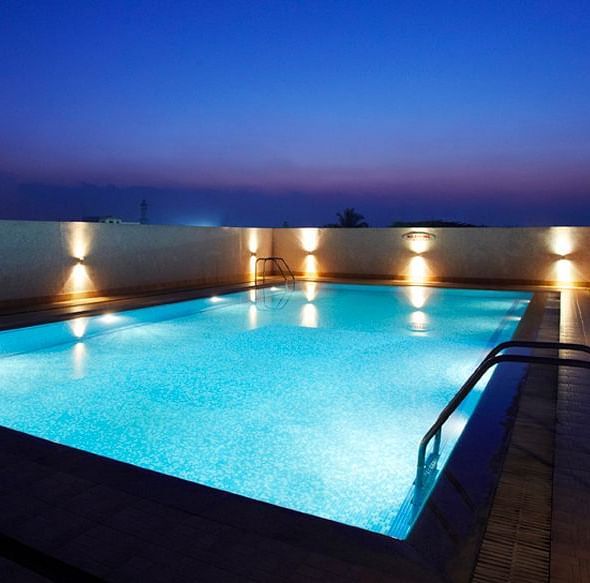 An image of an outdoor swimming pool installed with dim lights on the sides of it - Hotel Pai Vista, Mysore