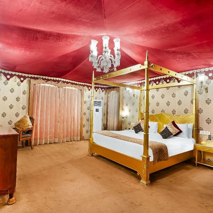 A lavishly decorated tent suite at the Rajasthali Resort & Spa in Jaipur features a four-poster bed, ornate furnishings, and a red draped ceiling.