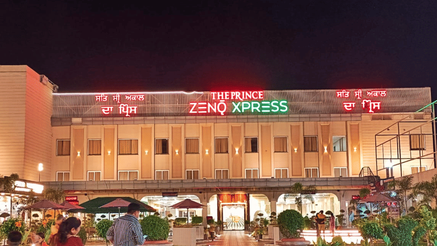 Illuminated facade of the Prince Zenq Xpress Resortt Rohtak, featuring guests entering the premises.