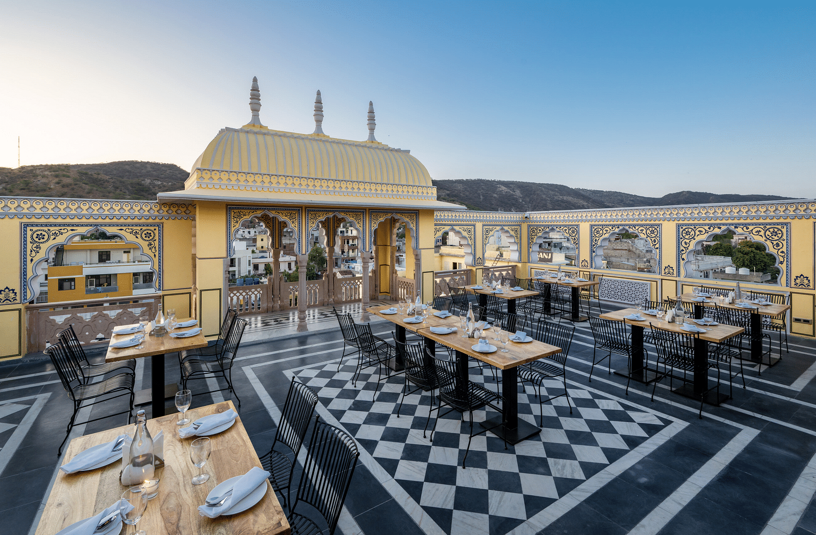 a roof top dining setup with beautiful views of the surrounding mountains and the early sunset - Brij Castle, Jaipur