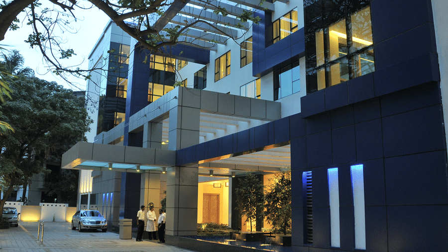 The exterior of a modern, multi-story building with blue and grey accents, illuminated at dusk - Adarsh Hamilton.