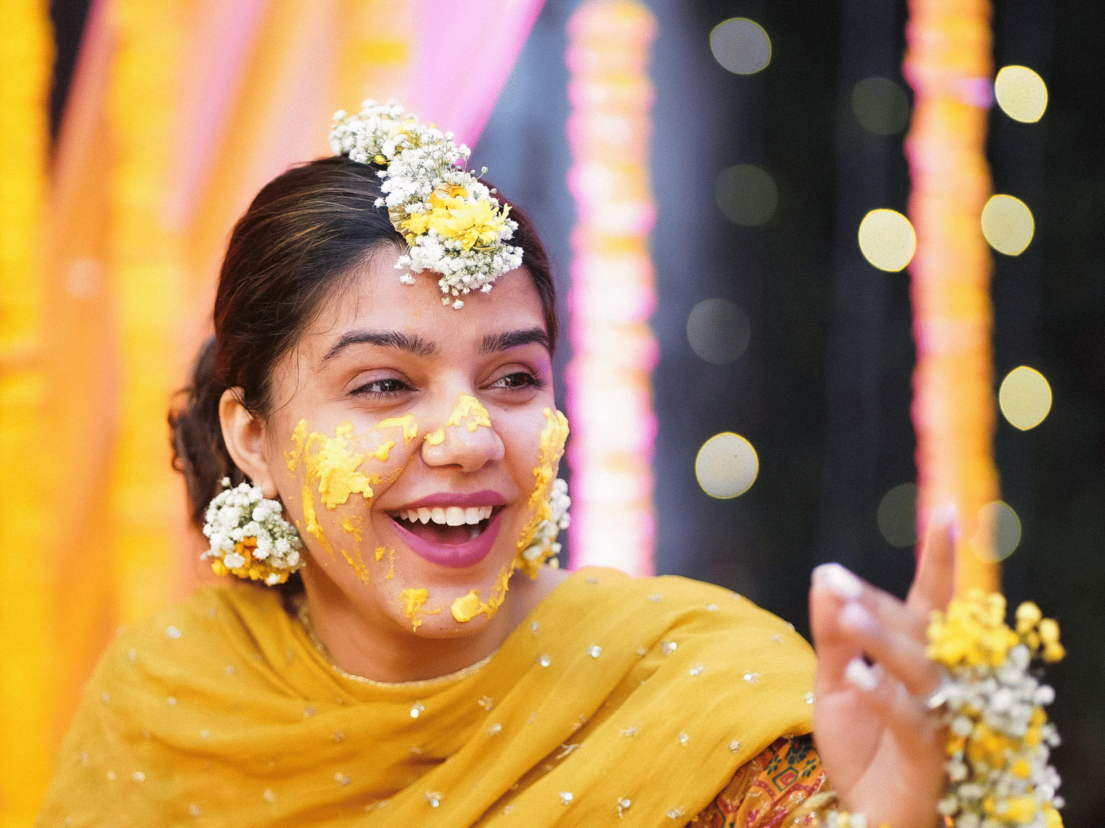 A smiling bride adorned with flowers and haldi during a joyful pre-wedding celebration.