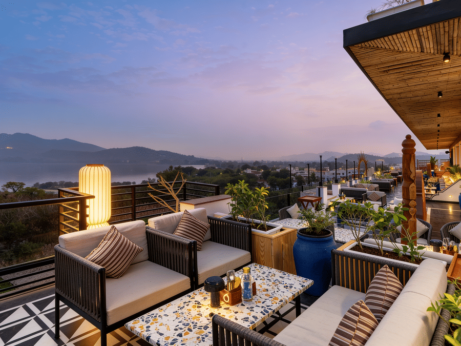 Armchairs and cushioned seating are arranged on a rooftop terrace at The Sierra - By The Lake, offering an open view of hills under an evening sky.