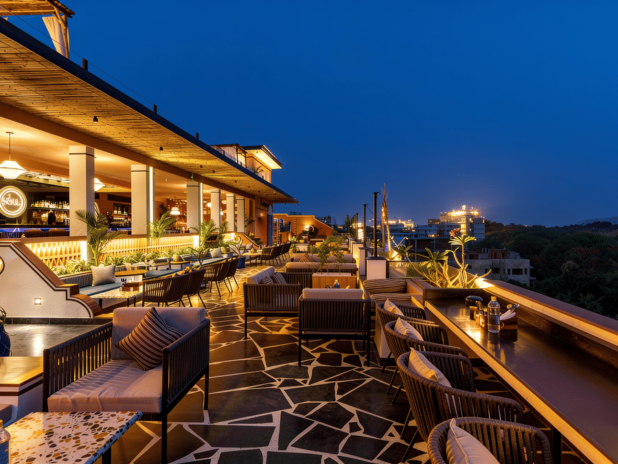 Small dining tables and chairs are illuminated at night on the outdoor rooftop terrace of The Sierra - By The Lake, with distant city lights visible.