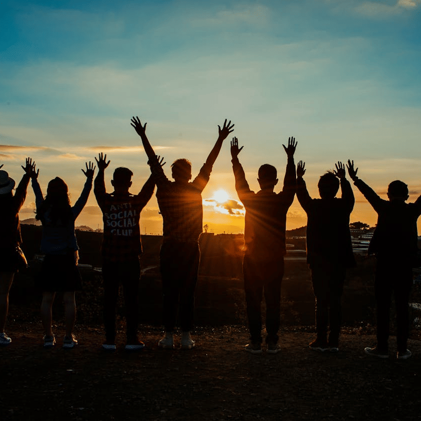 A silhouette of a group of people with raised hands, while watching the sun - Avianna Group of Hotels & Resorts