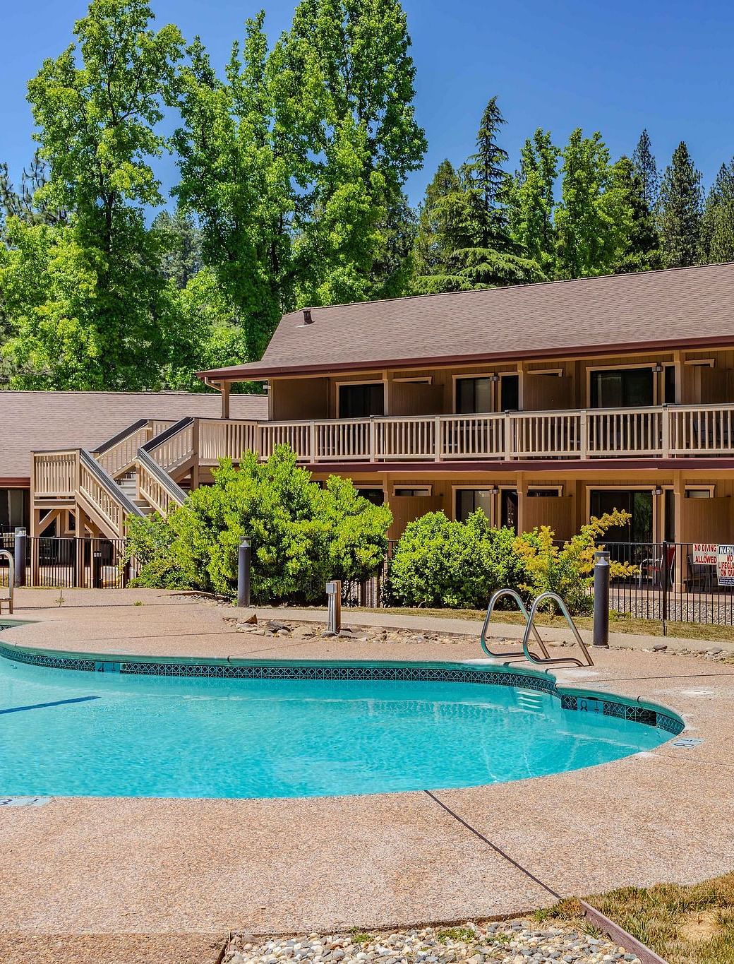 A view of an outdoor swimming pool with the hotel building in the backdrop on a clear, blue day - Amador Hotel.