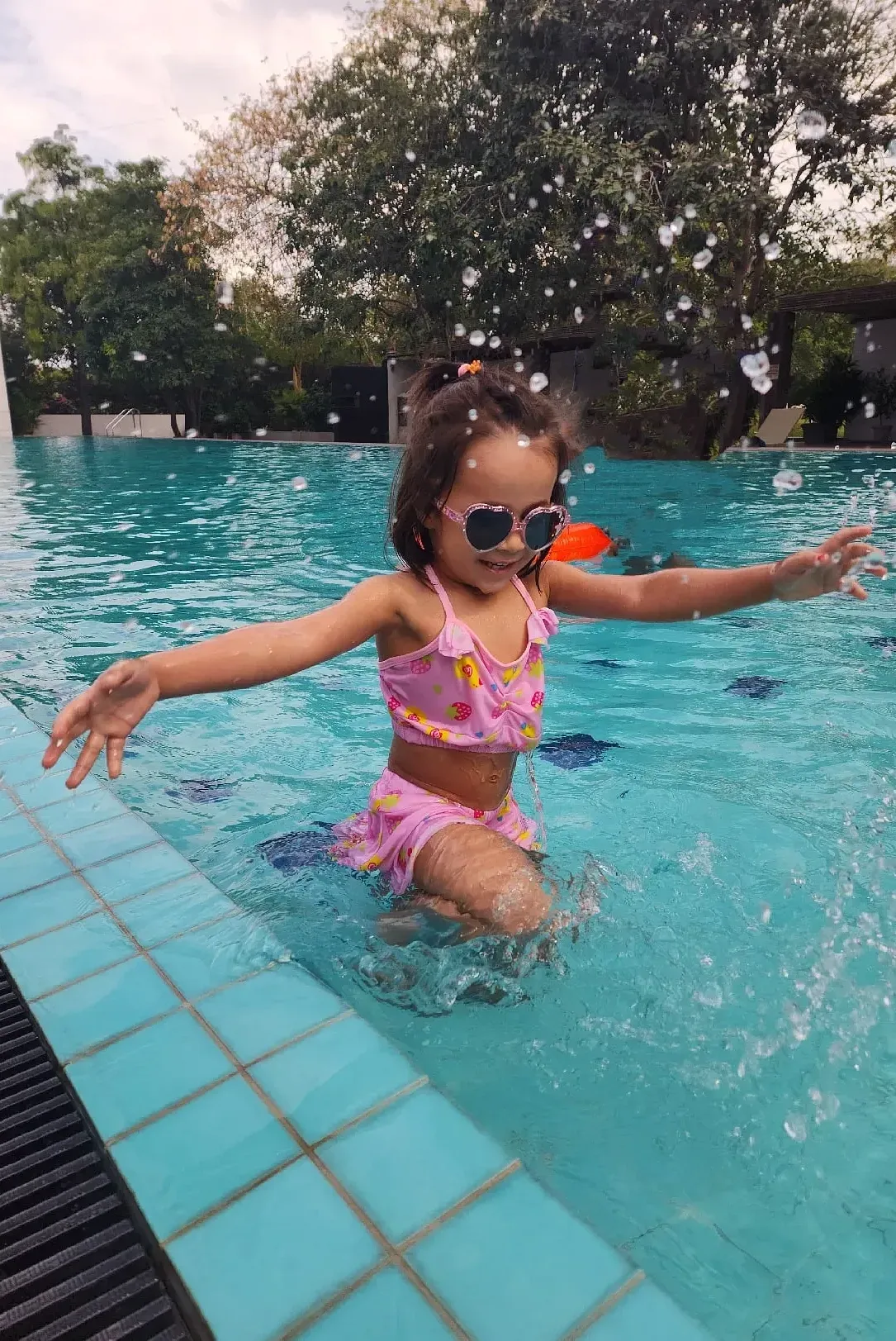 A girl in a swimming costume standing in a pool with arms raised at Karma Chalets.