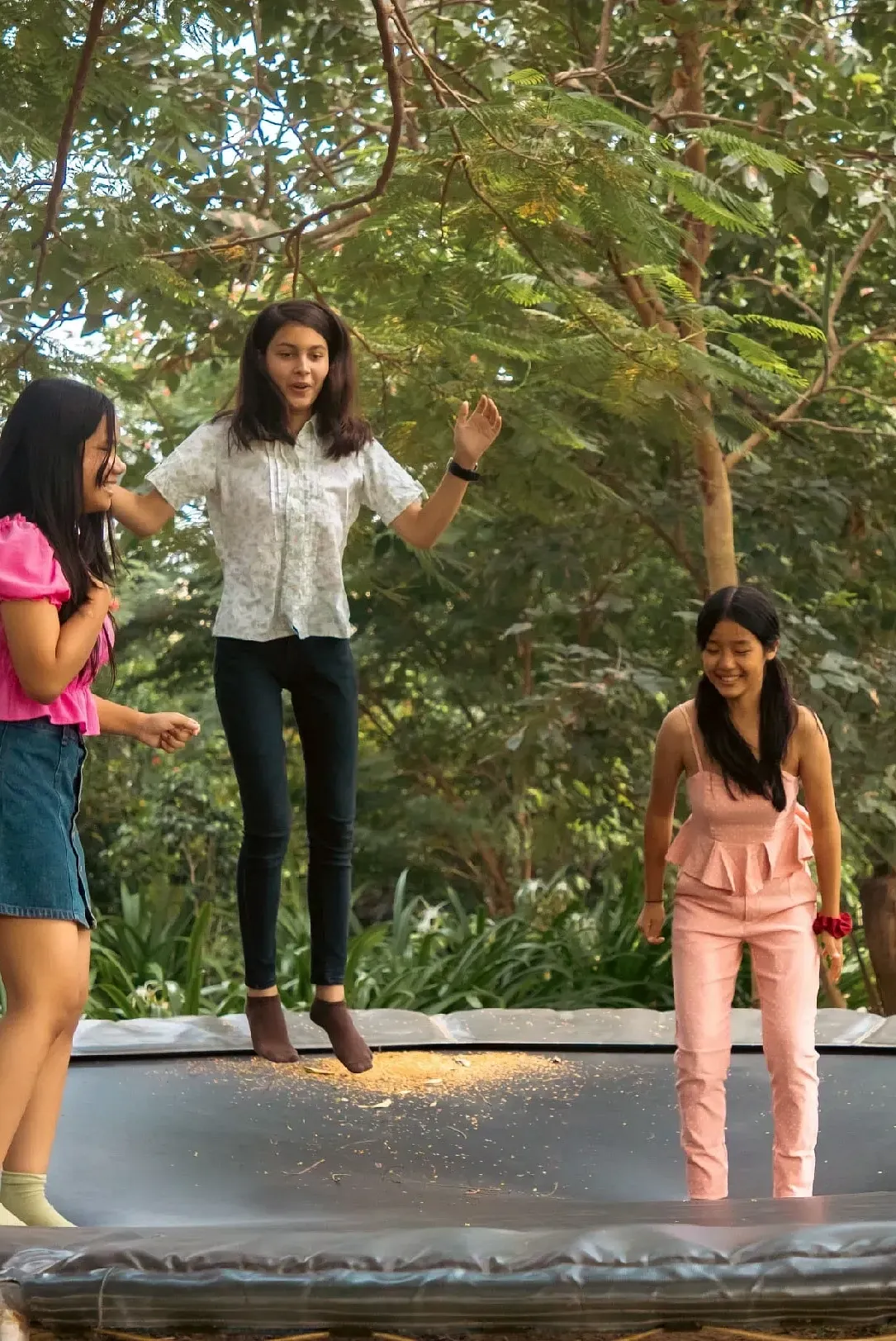 Three children standing on a trampoline outdoors near trees at Karma Chalets.